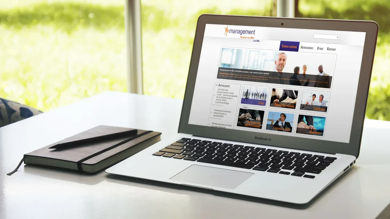 MacBook Air wyświetlający stronę HR Management na biurku z notatnikiem