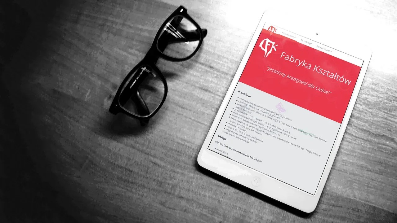 iPad wyświetlający stronę Fabryki Kształtów na drewnianym biurku z okularami