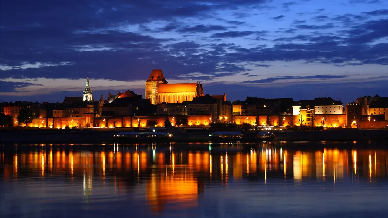 Night panorama of Toruń old town with illuminated cathedral and city walls reflected in the Vistula River